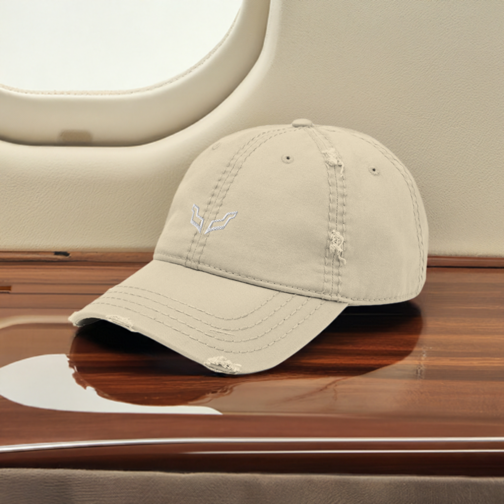 Velite Armor Premium Distressed Hat in beige, embroidered logo, placed inside a private jet for a sophisticated, high-end luxury aesthetic