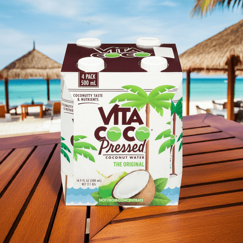 Vita Coco Pressed Coconut Water with Pulp 4-pack on tropical deck with beach view, refreshing natural hydration drink.