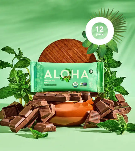 Aloha Chocolate Mint Protein Bar 12-pack surrounded by dark chocolate pieces and fresh mint leaves on a green background. USDA Organic, Non-GMO, and vegan certified snack.