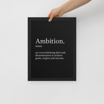 Close-up of a person hanging a black motivational poster titled "Ambition" on a wall.