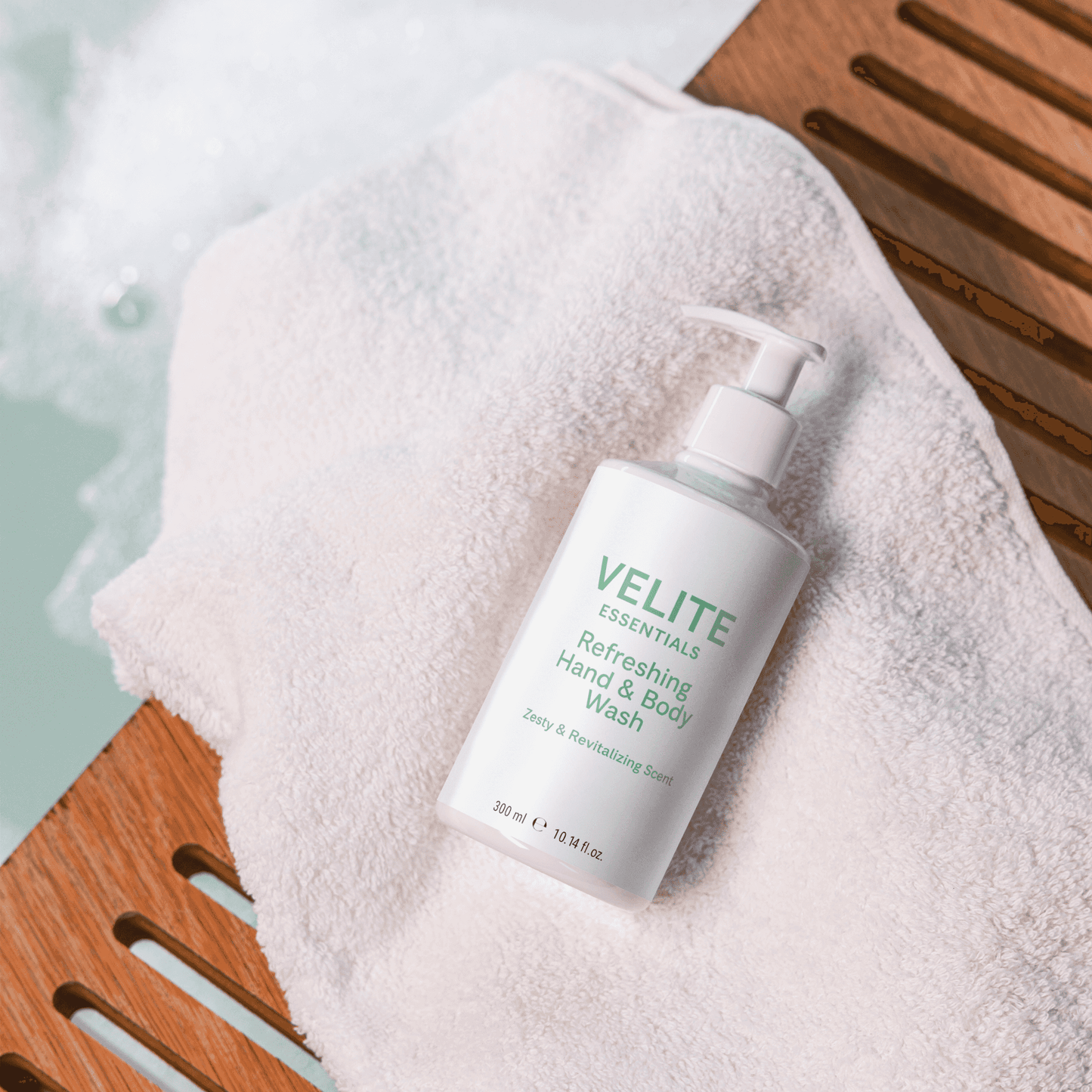 Velite Essentials Citrus Fresh Body Wash placed on a towel by a bath, perfect for daily moisturizing and gentle cleansing in a spa-like setting.