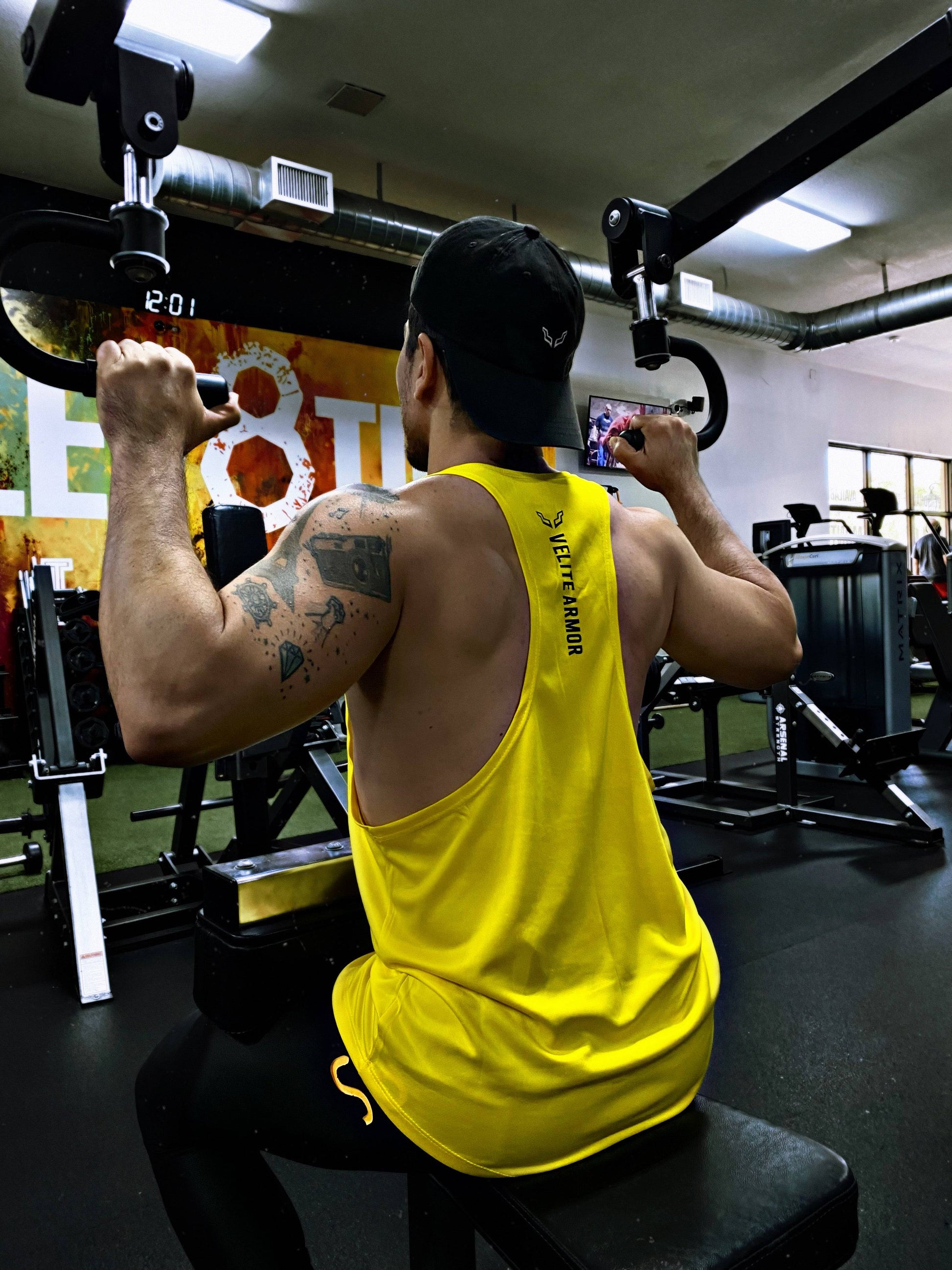 Back view of Yellow Booster Athletic Wear tank top by Velite Armor during lat pulldown, highlighting racerback cut and sweat-wicking performance.
