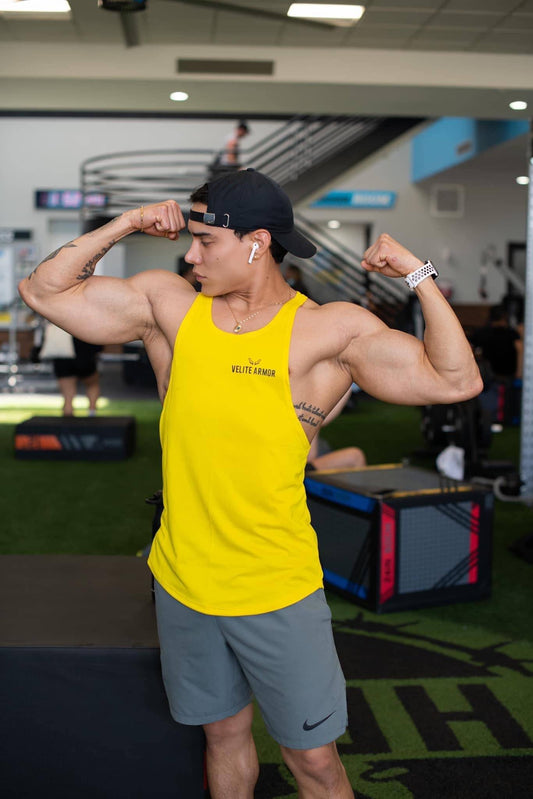 Yellow Booster Athletic Wear tank top by Velite Armor, featuring sweat-wicking fabric and durable design, worn during gym flex pose.